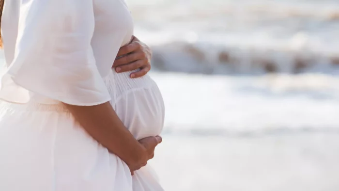 Pregnant woman holding on to her bump on the beach